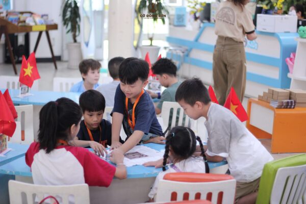 Năm em nhỏ chụm đầu cùng nhau setup và chơi Cờ Đông Sơn trên bàn .