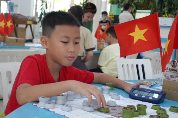 Kỳ thủ nhí áo đỏ tập trung dứt khoát đi quân và thao tác với đồng hồ thi đấu trong buổi sinh hoạt Cờ Đông Sơn.
