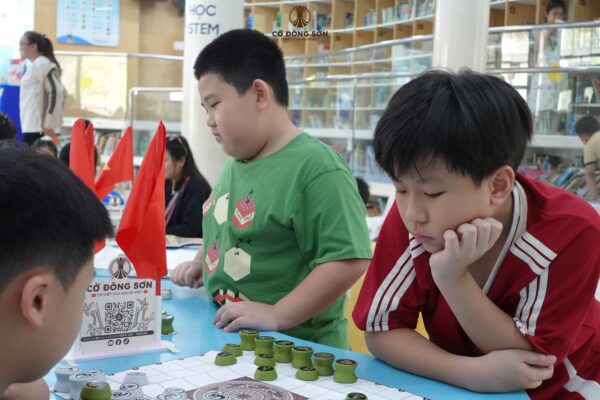Kỳ thủ nhí áo đỏ chống cằm suy nghĩ nước đi chiến thuật vô cùng chăm chú trong buổi sinh hoạt Cờ Đông Sơn.