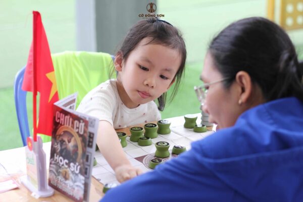 Hình ảnh cận cảnh bé gái đang tập trung cao độ di chuyển quân Cờ Đông Sơn trong ván đấu cùng phụ huynh tại sự kiện Đường sách TP. Thủ Đức.