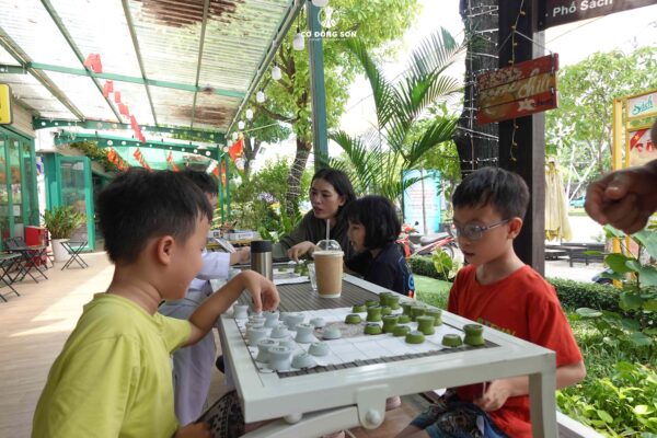 Các bé trai đang say sưa chơi Cờ Đông Sơn cùng phụ huynh trong không gian cà phê xanh mát tại Đường sách TP. Thủ Đức