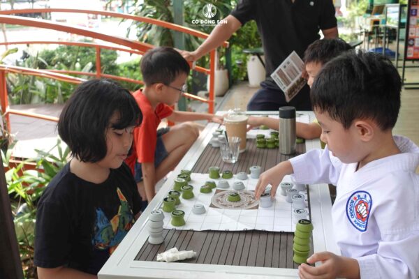 Cận cảnh bé trai mặc võ phục Karate đang tập trung cao độ khi chơi board game Cờ Đông Sơn cùng bạn tại Đường sách TP. Thủ Đức.