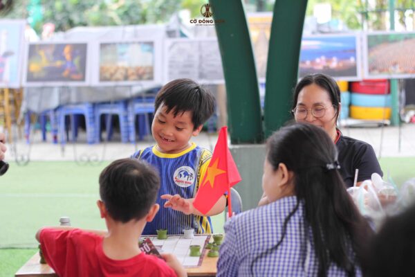 Nụ cười rạng rỡ và thích thú của bé trai khi trải nghiệm ván Cờ Đông Sơn cùng bạn bè và phụ huynh tại sự kiện Đường sách TP. Thủ Đức.