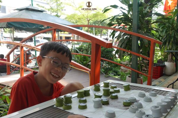 Nụ cười sảng khoái đầy thích thú của bé trai khi đang trải nghiệm ván đấu Cờ Đông Sơn tại khuôn viên Nhà Sách Thái Hà, Đường Sách TP. Thủ Đức.