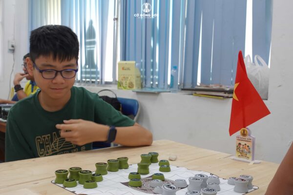 Thiếu niên đeo kính đang tập trung cao độ, suy nghĩ nước đi chiến thuật trên bàn Cờ Đông Sơn trong buổi sinh hoạt tại CLB Lam Sơn.