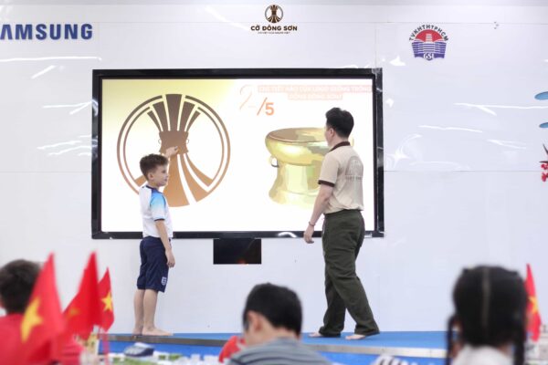 ậu bé tự tin chỉ vào màn hình lớn giải đáp ý nghĩa hình ảnh trống đồng trên logo trong giờ học lý thuyết tại Khóa hè Cờ Đông Sơn.