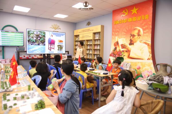 Các học viên nhí đang chăm chú quan sát màn hình bài giảng so sánh hình dáng quân cờ với các loại trống truyền thống tại Khóa hè Cờ Đông Sơn.
