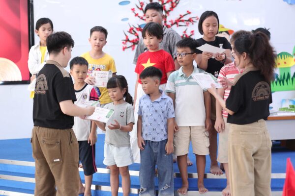 Huấn luyện viên đang ân cần trao tận tay giấy chứng nhận hoàn thành khóa học cho các kỳ thủ nhí trên bục sân khấu lễ bế giảng Khóa hè Cờ Đông Sơn.