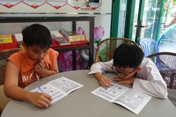 Cận cảnh hai học viên nhí đang say sưa suy nghĩ và làm bài tập lý thuyết trong sổ tay bài tập tại Khóa hè Cờ Đông Sơn.