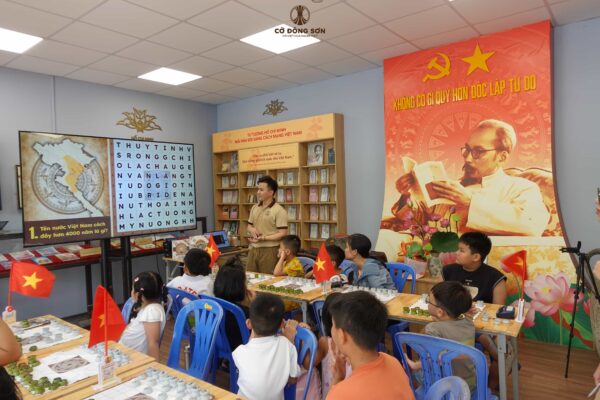 Huấn luyện viên đang hướng dẫn các học viên nhí giải ô chữ lịch sử về thời kỳ Hùng Vương trong buổi sinh hoạt của Khóa hè Cờ Đông Sơn.